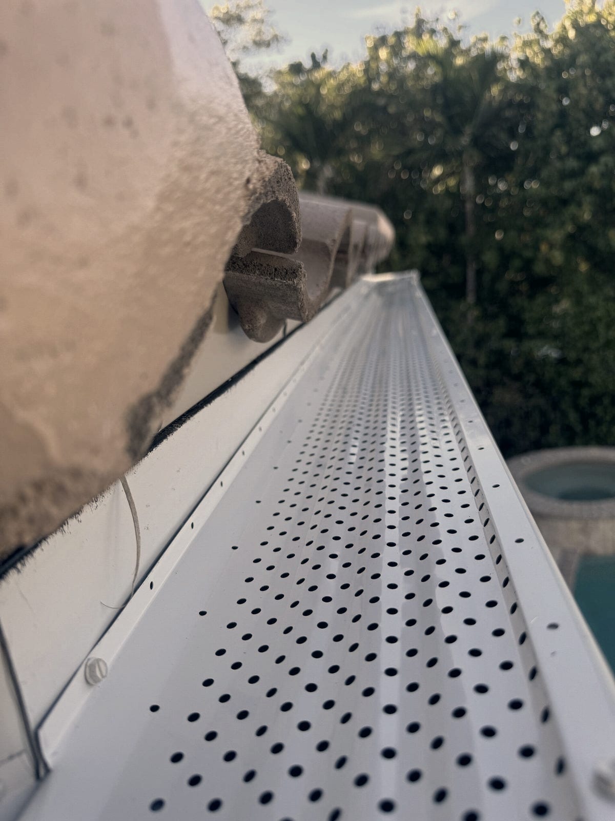 A perforated leaf guard covers the full length of a white gutter at the edge of a barrel tile roof.